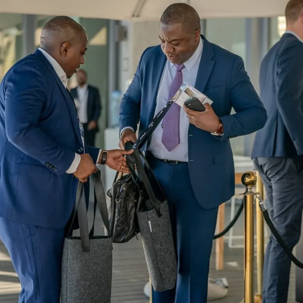 Two delegates in suits carrying grey RPET felt conference bags
