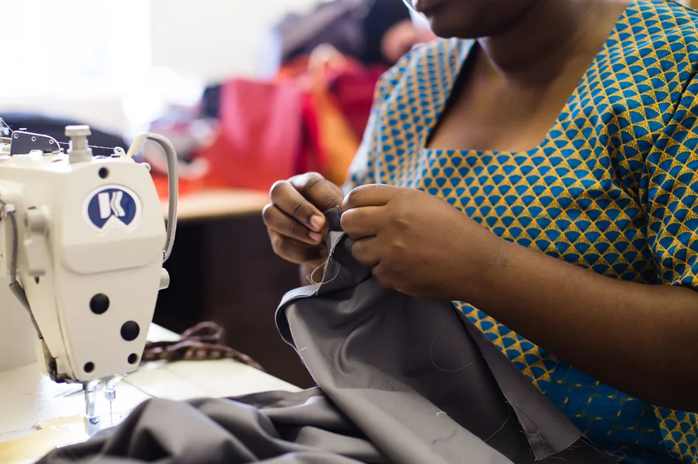 Seamstress in shweshwe-patterned dress sewing a bag at the Cape Town workshop